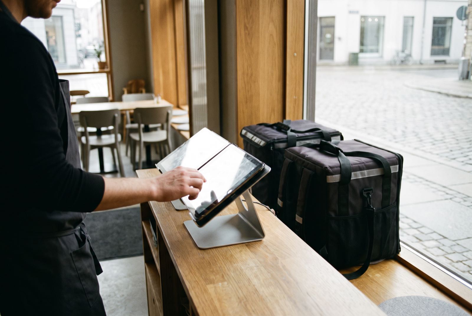 Staff updating the menu on the POS tablet with packed delivery bags beside it